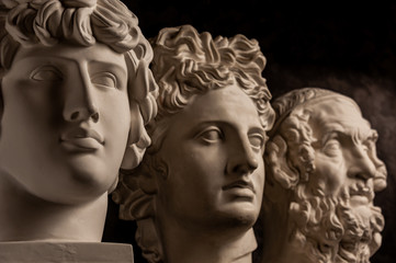 Group gypsum busts of ancient statues human heads for artists on a dark background. Plaster sculptures of antique people faces. Renaissance epoch style. Academic subject. Blank for creativity.