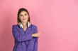 With headphones, pointing. Caucasian young woman's portrait on pink studio background. Beautiful female model in purple jacket. Concept of human emotions, facial expression, sales, ad. Copyspace.