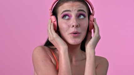 Wall Mural - Young amazing emotional woman isolated over pink wall background listening music with headphones