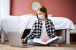 © khmelev - Girl in protective medical mask sitting on the floor with laptop and cominacate with teacher via online application. Distance learning online education.