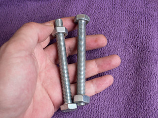 Bolt and nut in male workers hands isolated on purple background