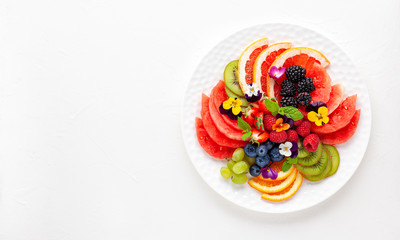 Wall Mural - Delicious healthy salad of fresh fruits, berries and edible flowers on white plate. Clean eating. Top view.