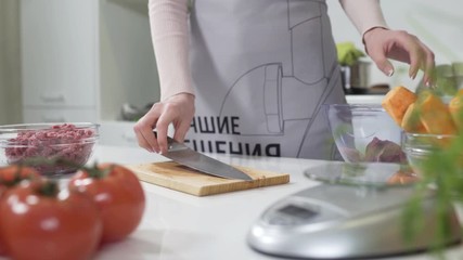 Wall Mural - Woman cutting raw meat on small pieces with kitchen knife cutting board. Female cutting red beef filet on wooden board, holding knife in hand. Housewife is cooking at home interior. Concept: food