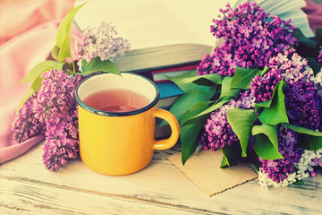 Wall Mural - Bouquet of a lilac, a yellow сup and books оn wooden background, toned.