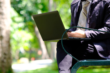 Businessman working with laptop computer and using his phone outdoors