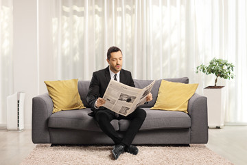 Wall Mural - Man in a formal suit sitting on a sofa and reading a newspaper in a living room