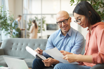 Wall Mural - portrait of bald mature businessman smiling at asian young woman while discussing project in modern 