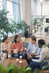 Wall Mural - High angle view at multi-ethnic group of young people eating takeout food and enjoying chatting during lunch break in office, copy space