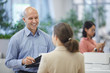 © Seventyfour - Waist up portrait of bald mature businessman smiling happily while talking to female colleague or secretary standing in modern office interior, copy space