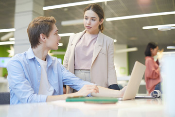 Wall Mural - portrait of young man explaining work project to female colleague while using laptop in office, copy