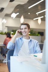Wall Mural - portrait of smiling young man lspeaking by smartphone while working with laptop in office