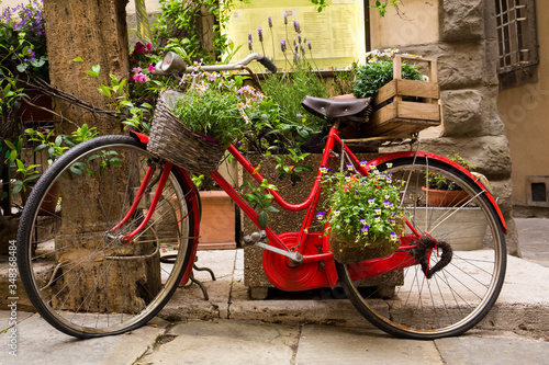 Classic red bike adorned with flowers, basket and wine crate in Cortona, a hill town in the Tuscany region of Italy