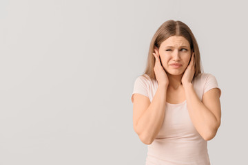 Canvas Print - Young woman suffering from loud noise on light background