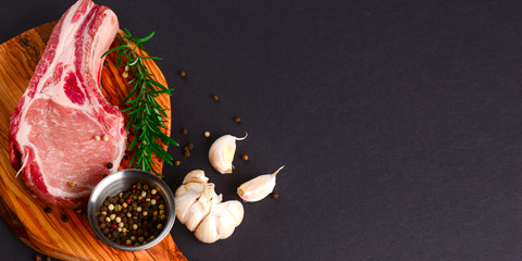 Fresh raw beef steak on wooden cutting board over black background with spices, top view.