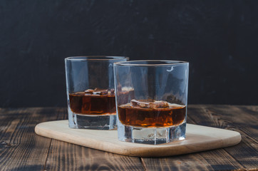 Wall Mural - Two Glasses of whiskey with ice cubes on a wooden table/Two Glasses of whiskey with ice cubes on a wooden table. Black background with copyspace.