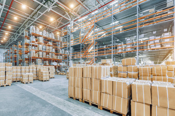 Large industrial warehouse with high racks. In the foreground are a lot of cardboard boxes.