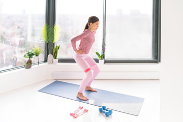 Resistance band fitness home workout woman doing squats exercises using loop bands for leg glutes standing exercise with strap elastic. Glute muscle activation for thighs cellulite.