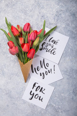 Wall Mural - red  beautiful tulips in an ice cream waffle cone with card Hello you on a concrete background. Conceptual idea of a flower gift. Spring mood