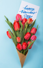 red  beautiful tulips in an ice cream waffle cone with card Womans Day on a concrete background. Conceptual idea of a flower gift. Spring mood