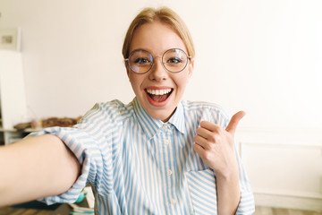 Photo of joyful woman showing thumb up while taking selfie photo