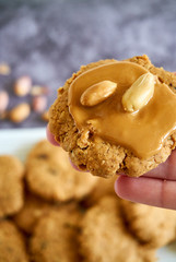 Women hand holding a homemade peanut butter cookie with natural peanut butter spread and tow peanuts on top of the cookie, healthy gluten-free cookie