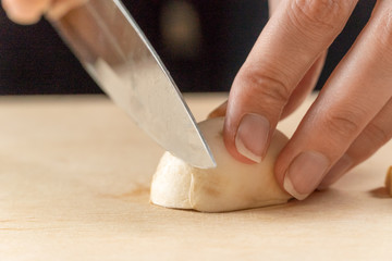 women's hands cut mushrooms on a wooden board close up