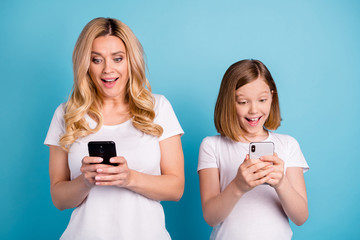 Sticker - Photo of two people beautiful mom lady little daughter excited mood spend leisure together hold telephones reading post bloggers wear casual white s-shirts isolated blue color background