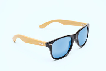 Trendy and fashionable modern sunglasses with wooden bows isolated on light blue background. Summer sunlight and UV protection optics concept