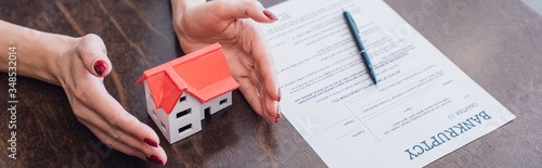 Fotografía Cropped view of female hands near house model, paper with bankruptcy lettering a