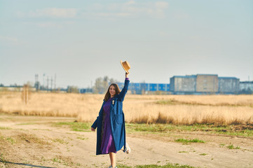 Happy young lady in blue coat with beige hat runs in field early spring.