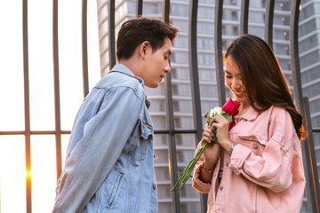 young couple love and romantic at first date.  asian teenage woman surprise and smiling at boyfriend gives rose flowers at dinner in valentine day. couple and happiness concept.