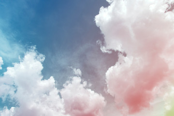 Colorful puffy fluffy cumulus clouds with gradient pink, purple & yellow colored on beautiful sunny blue sky in tropical summer or spring sunlight & sun rays, abstract surreal nature background 