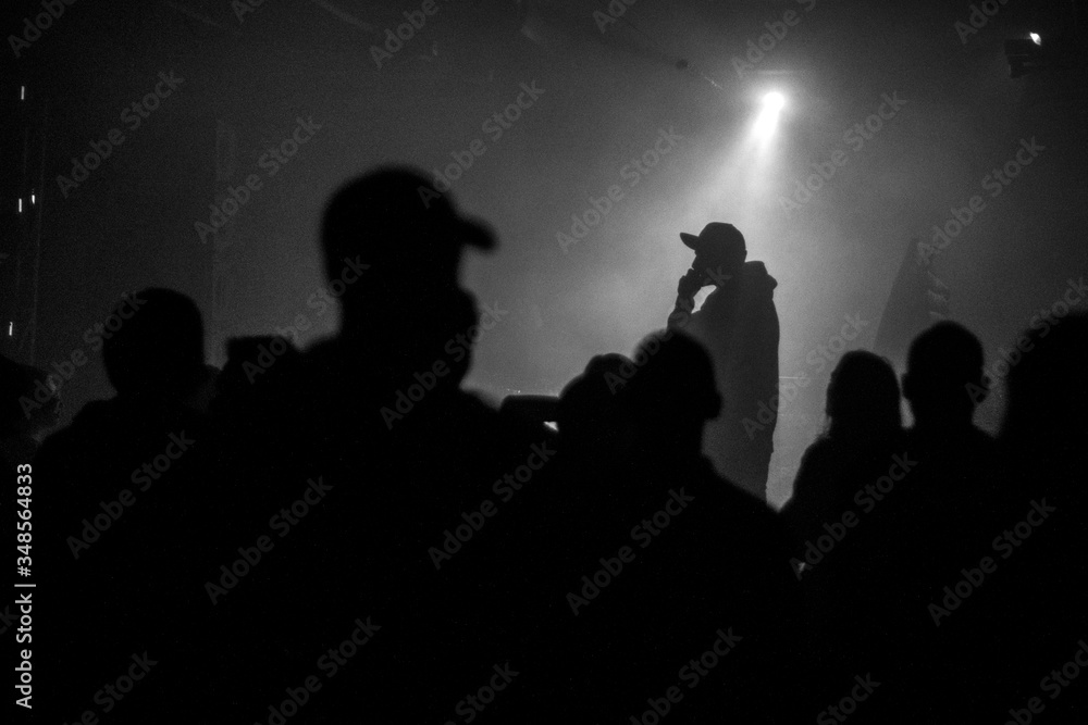 A silhouette of singer rap musician during live concert in dark light. Dark background, smoke, spotlights - obrazy, fototapety, plakaty 