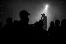 A Silhouette Of Singer Rap Musician During Live Concert In Dark Light. Dark Background, Smoke, Spotlights
