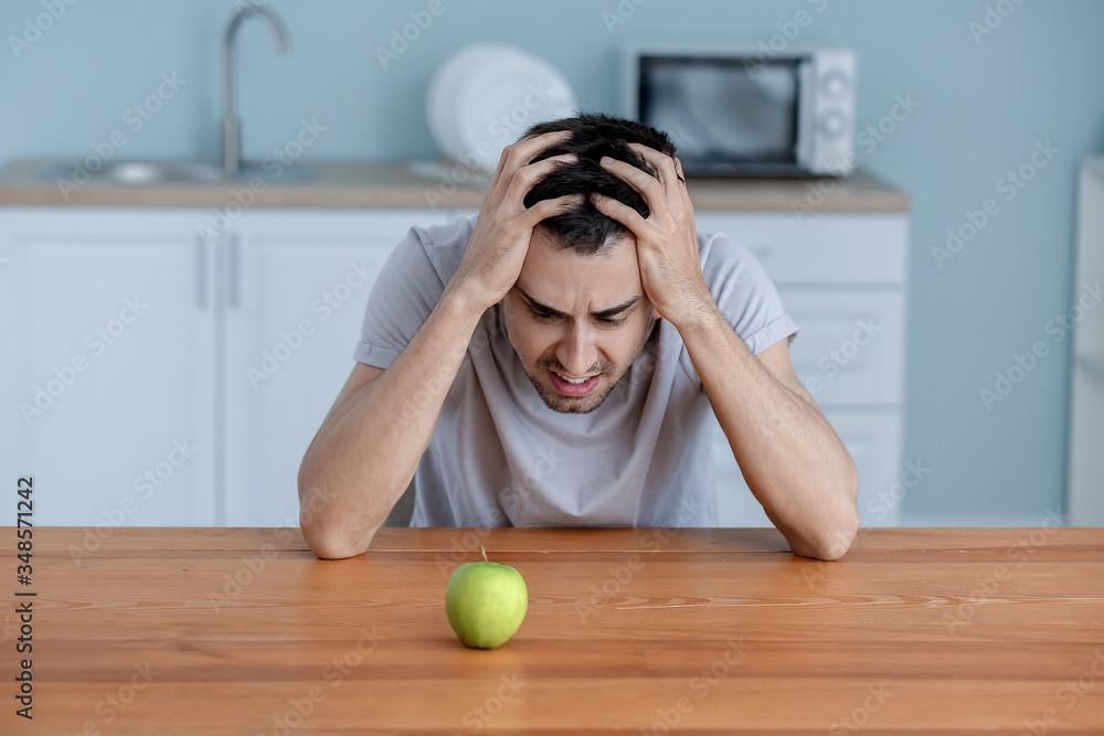 Young man suffering from anorexia with apple in kitchen