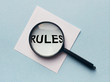 Magnifying glass or loupe with the word rules on a white memo note on blue background. Searching new rules