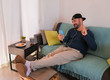 © Sabrina - Young happy man on a videocall with his family - Man is sitting on the couch with his smartphone and headset - Social contact in time of coronavirus - Isolated at home for the covid - 19