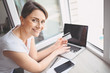 © Алина Троева - Beautiful happy woman holding credit card in hand and using laptop computer keyboard. Businesswoman or entrepreneur working. Online shopping, e-commerce, internet banking, spending money concept