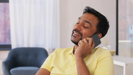 Canvas Print - technology, communication and people concept - happy smiling indian man calling on smartphone and resting feet on table at home office