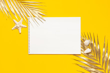 Flat Lay Summer Background. Open Notebook With Clean White Pages On A Spiral, Golden Tropical Leaves, Shells Starfish On Yellow Background Top View Copy Space. Summer Beach Template For Design