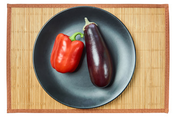 Wall Mural - purple eggplant and red bell pepper on a gray plate on a cane tablecloth