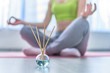 Fitness woman in lotus pose with aroma sticks and essential oil bottle during yoga training, aromatherapy treatments and meditation. Mental health
