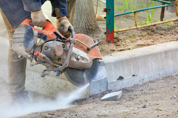 Worker at a construction site using a concrete saw cuts concrete curbs.