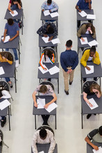 Teacher Supervising High School Students Taking Exam At Desks