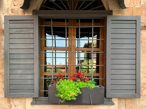 A window with flower pot, metal grill and  wooden shutters of an historical stone house in old town of Antalya Kaleici, Turkey. Horizontal stock image.