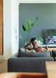 © Paul Bradbury/Caia Image - Young woman with remote control watching TV on living room sofa