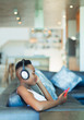 © Paul Bradbury/Caia Image - Young woman listening to music with headphones and mp3 player on sofa
