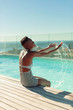 © Paul Bradbury/Caia Image - Carefree young woman splashing water at sunny swimming pool