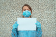 portrait of young blonde woman wearing a blue hay shirt protective gloves and a protective mask holding a white sheet of paper.