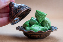 Religious Islamic Ramadan Concept: Closeup Of Sweet Nostalgic Green Peppermint Rock Candies (akide) In A Copper Like Traditional Bowl. Hand Holding Ornate Cap On Brown Background For Holidays (bayram)